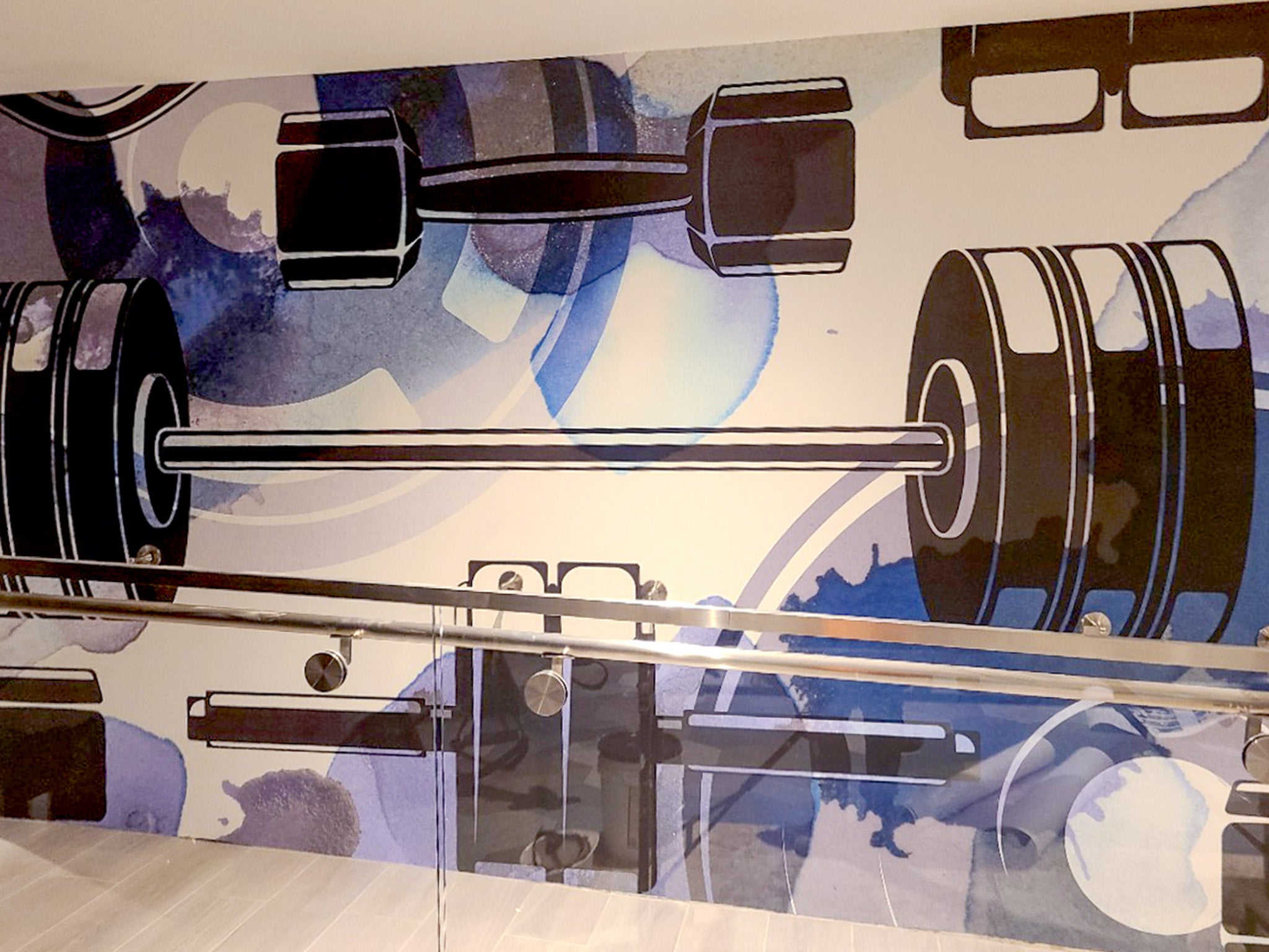 A section of Wrapped Studio’s custom gym mural in a multifamily building, featuring bold illustrations of weightlifting equipment in blue and gray tones.