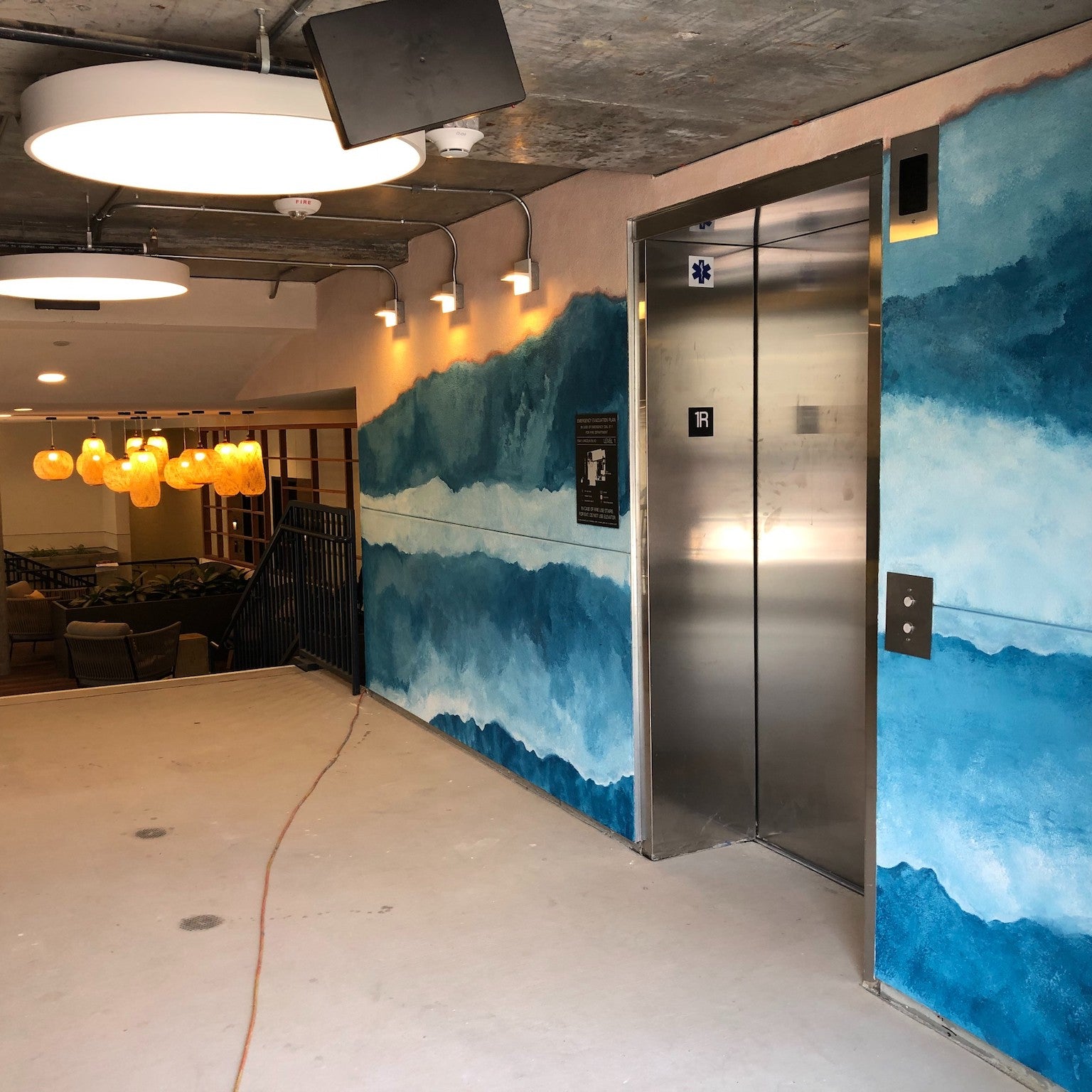 Elevator lobby at 1641 Lincoln with WRAPPED Studio's hand-painted mural, blending oceanic blues to guide and intrigue tenants with its watercolor effects.
