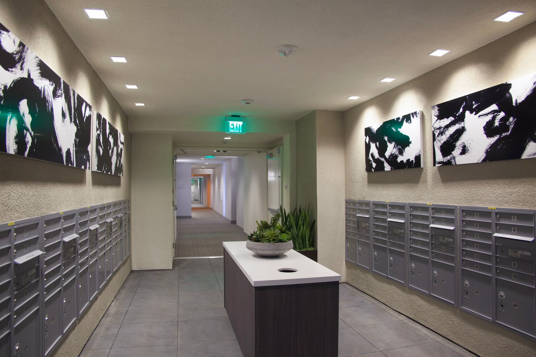 Modern mailroom in Alexan Aspect luxury residence with rows of silver mailboxes and abstract black and white brushstroke canvases by WRAPPED Studios on the walls.