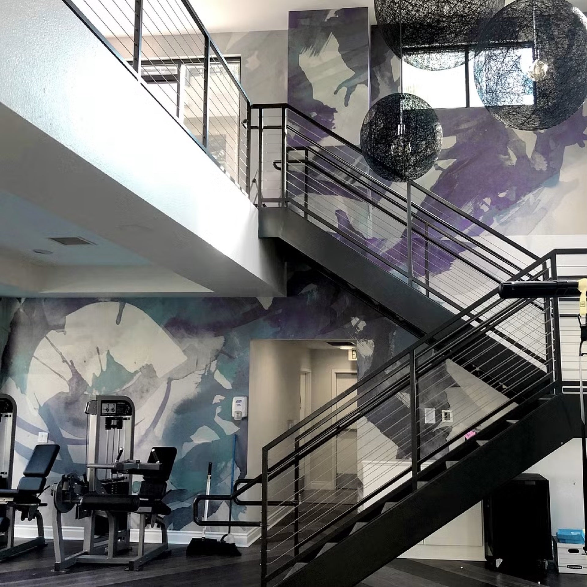 Staircase and gym area of a multifamily apartment complex with a large custom wallcovering featuring abstract purple and blue splashes, creating a dynamic and artistic space for residents.