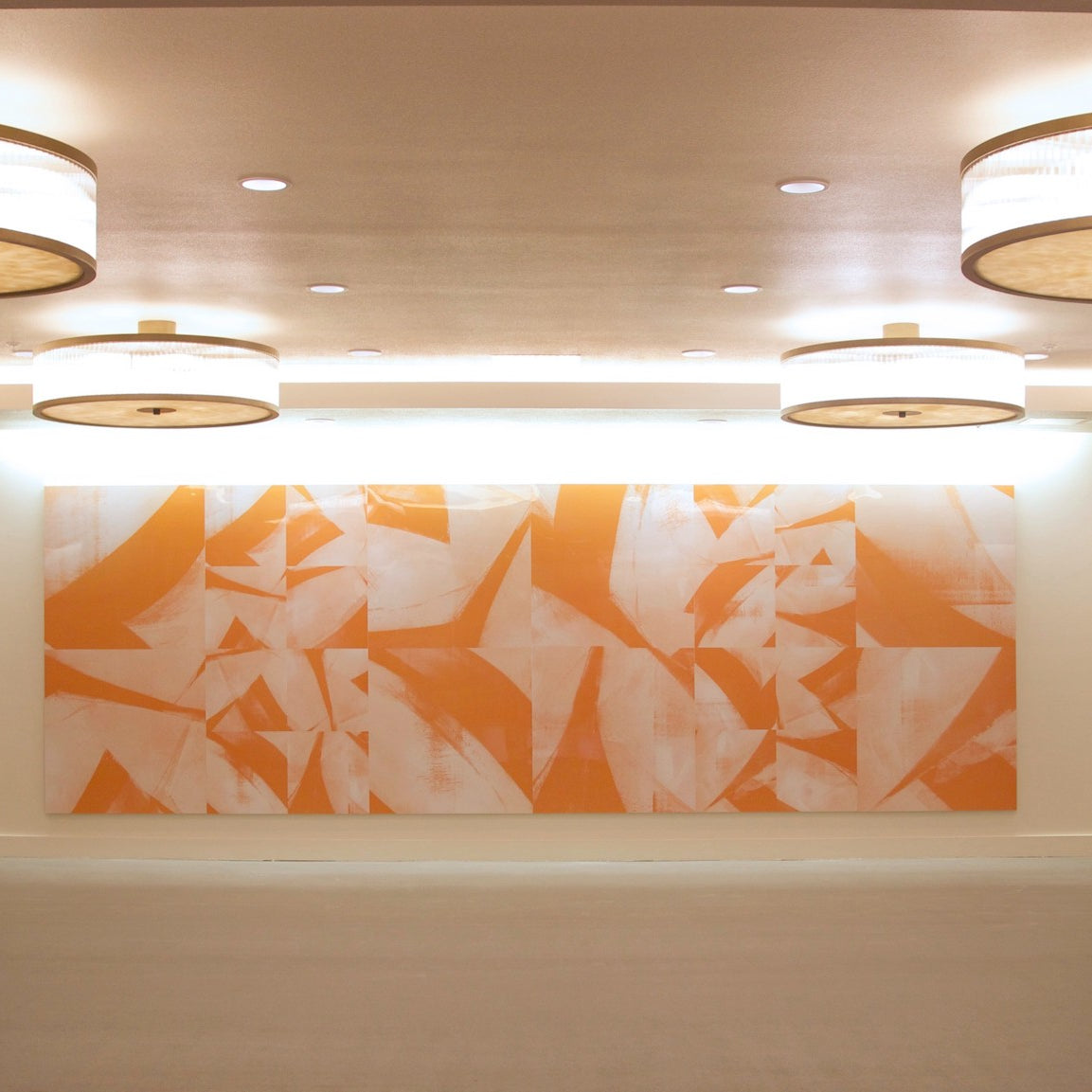 Entryway of Centerpointe motorcourt illuminated by large circular light fixtures, showcasing a warm-toned abstract geometric mural, inviting a sense of modern elegance.