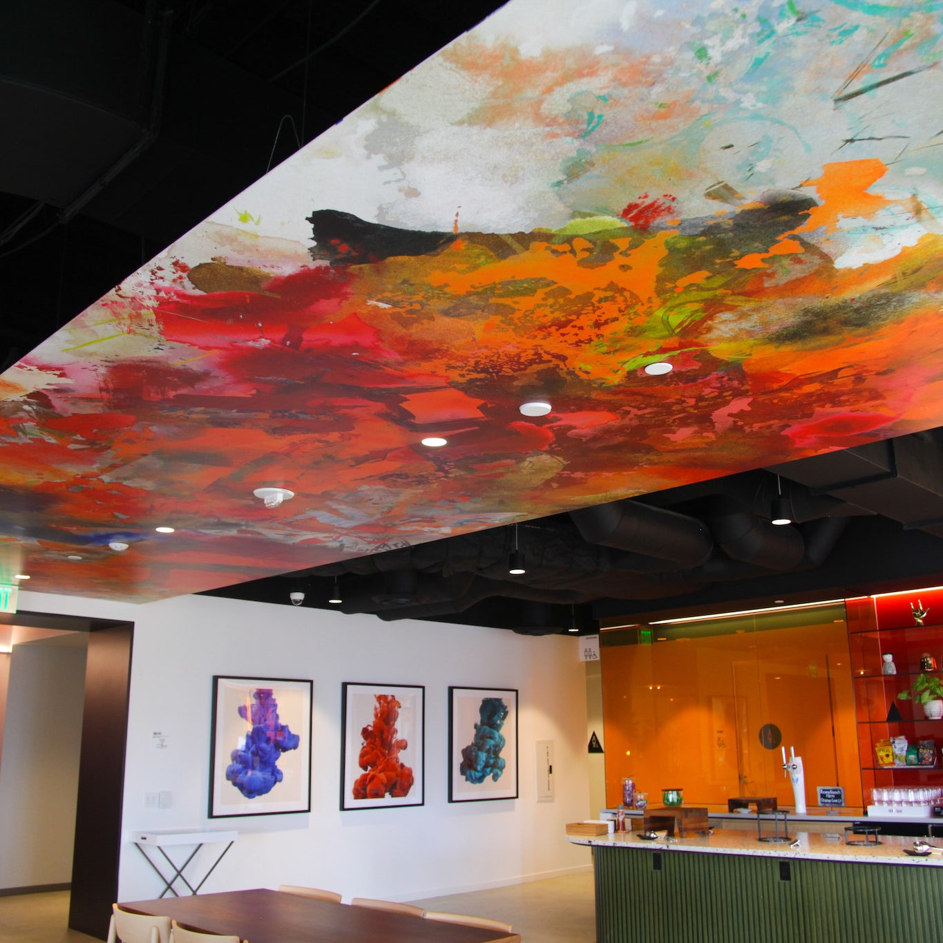 Convene DTLA's café corner under a vivid, large-scale wallcovering with warm color splashes, designed by WRAPPED Studio.