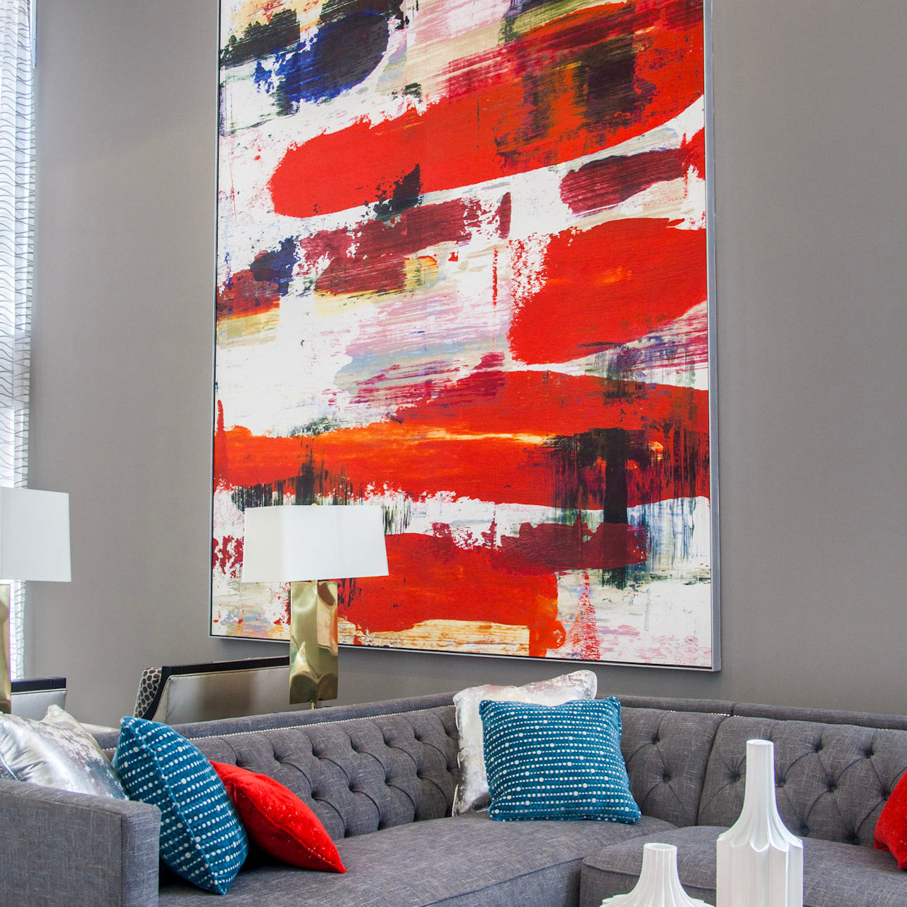 An abstract painting with bold brushstrokes in red, blue, and white dominates the lobby of Next on Sixth Apartments, complementing the sleek grey couch and vibrant throw pillows, contributing to the stylish atmosphere.