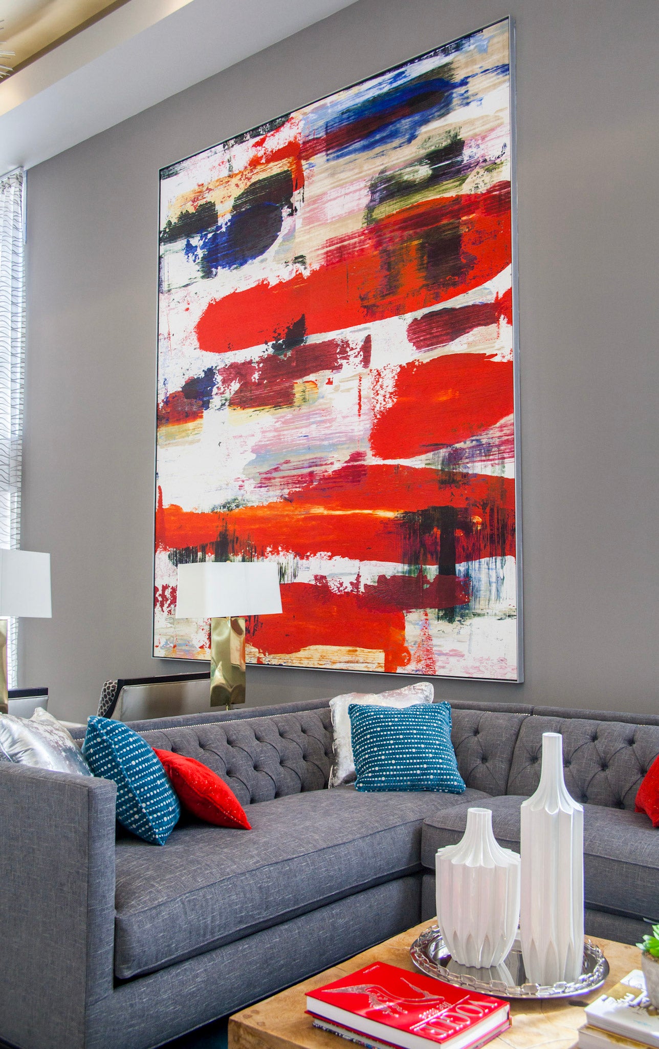 An abstract painting with bold brushstrokes in red, blue, and white dominates the lobby of Next on Sixth Apartments, complementing the sleek grey couch and vibrant throw pillows, contributing to the stylish atmosphere.