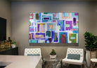 The lounge area in Next on Sixth Apartments is accentuated by an abstract geometric canvas art piece with a colorful palette of purples, blues, and greens, providing a lively focal point above the white tufted seating.