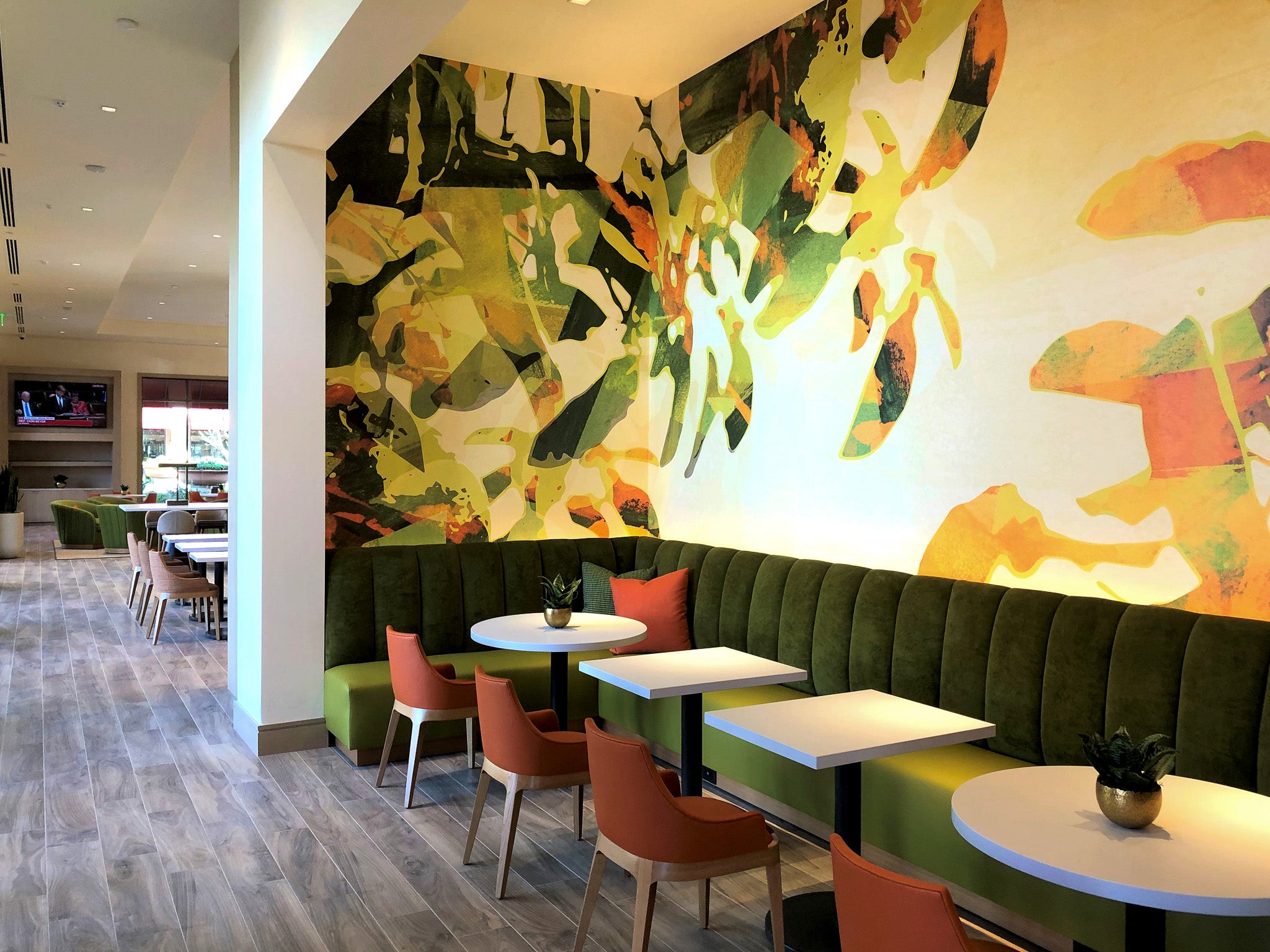 A custom large-scale wallcovering designed by WRAPPED Studio installed in the Promenade luxury apartment community in Orange County. The vibrant, nature-inspired mural enhances the upscale lounge area with abstract botanical forms in earthy greens, yellows, and oranges.
