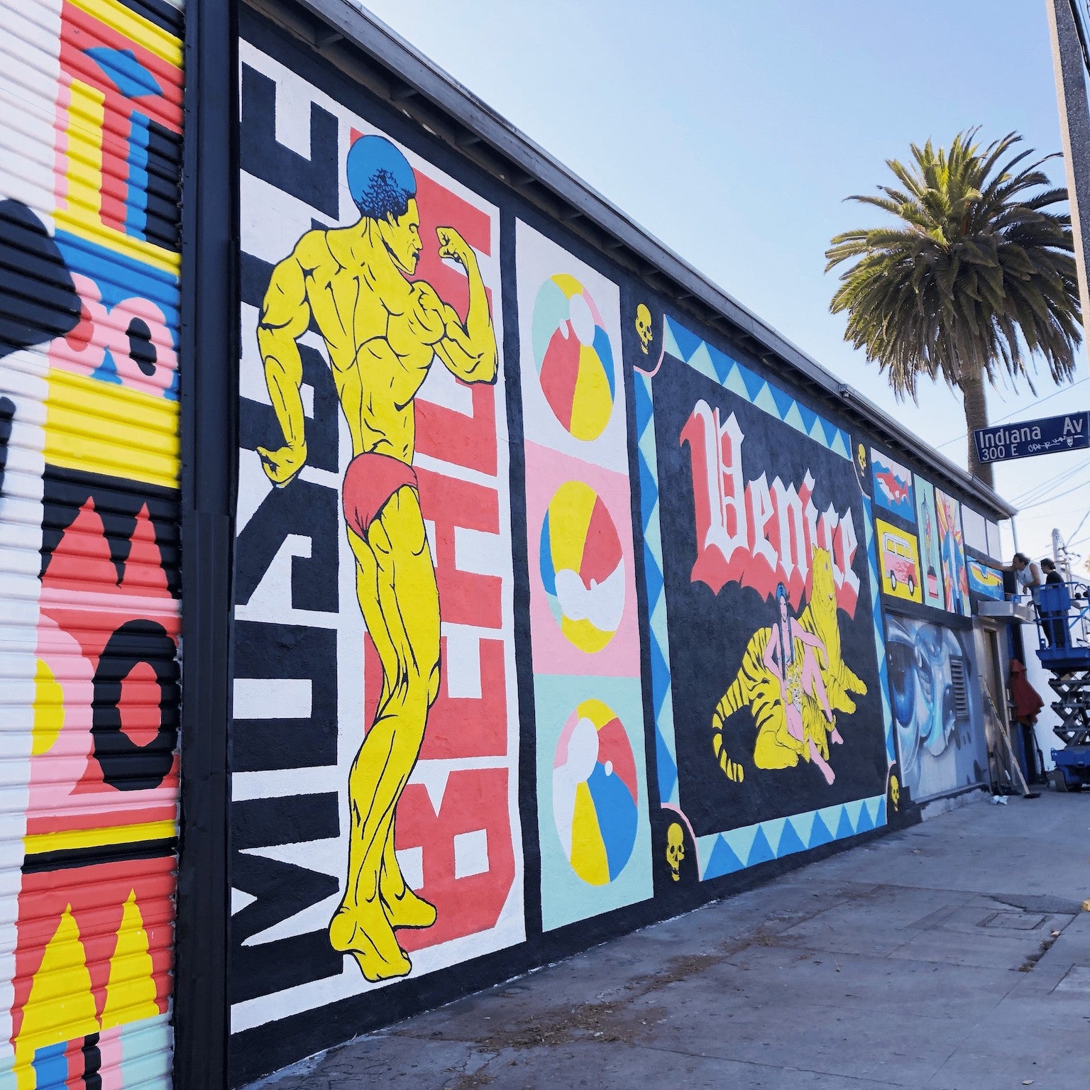 Colorful street mural by WRAPPED Studio on the exterior of Charles Arnoldi's art studio in Venice, featuring a dynamic collage of local icons, including a depiction of Arnold Schwarzenegger.