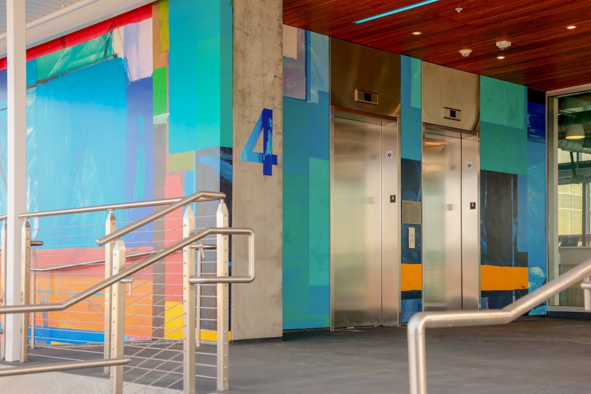 Bold blue and teal geometric mural by WRAPPED Studio framing elevator bays in a parking garage.
