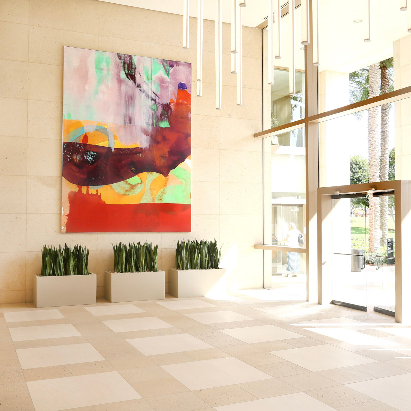 The grand foyer of 300 Spectrum Center decorated with a colorful custom artwork canvas with warm hues, creating a striking contrast with the elegant travertine walls and clean geometric lines of the space.