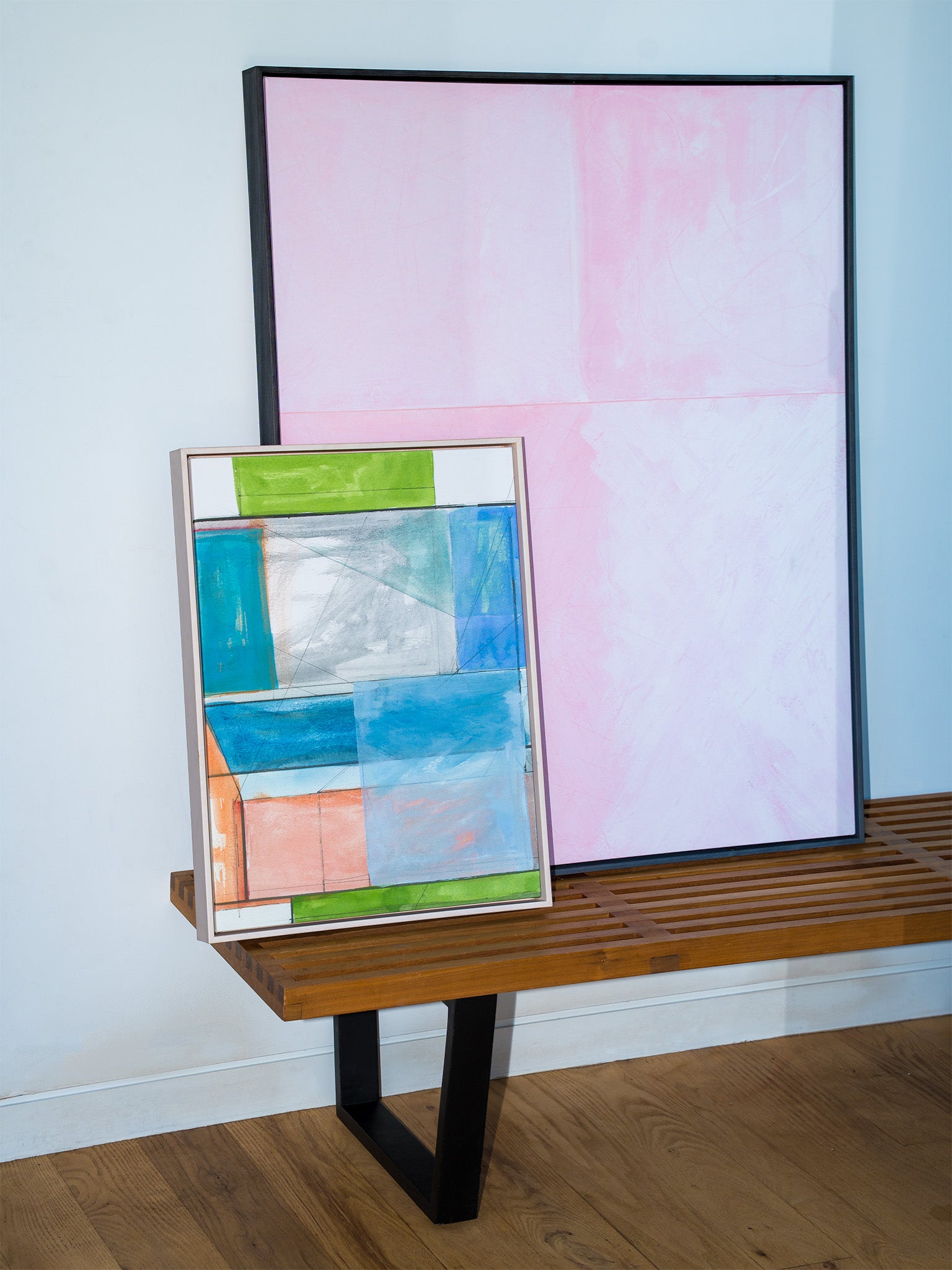 Two abstract artworks on a wooden shelf against a light blue wall. all-groups