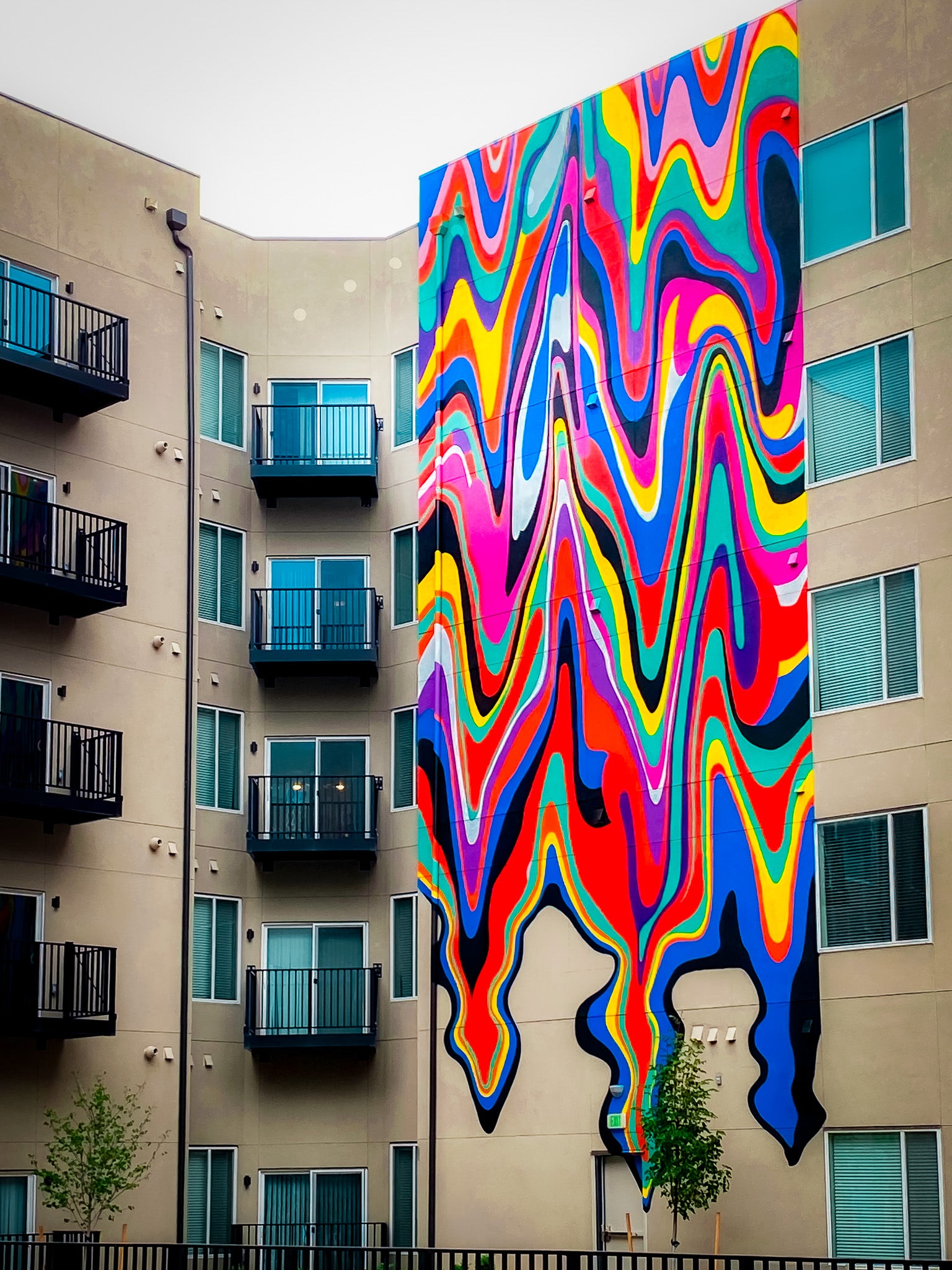 Colorful abstract mural with dripping, wave-like forms by WRAPPED Studio, painted on the exterior facade of Parkside City Center in Aurora, Colorado.